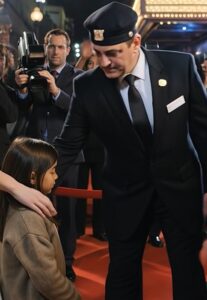 Kamery śledziły ją jak niechciane zakłócenie — aż do chwili, gdy mała dziewczynka uniosła nadgarstek, a twarz aktorki zastygła jak kamień.